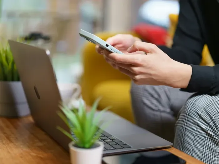 Person in business attire holding smartphone with laptop and plant on desk in Town Directory List